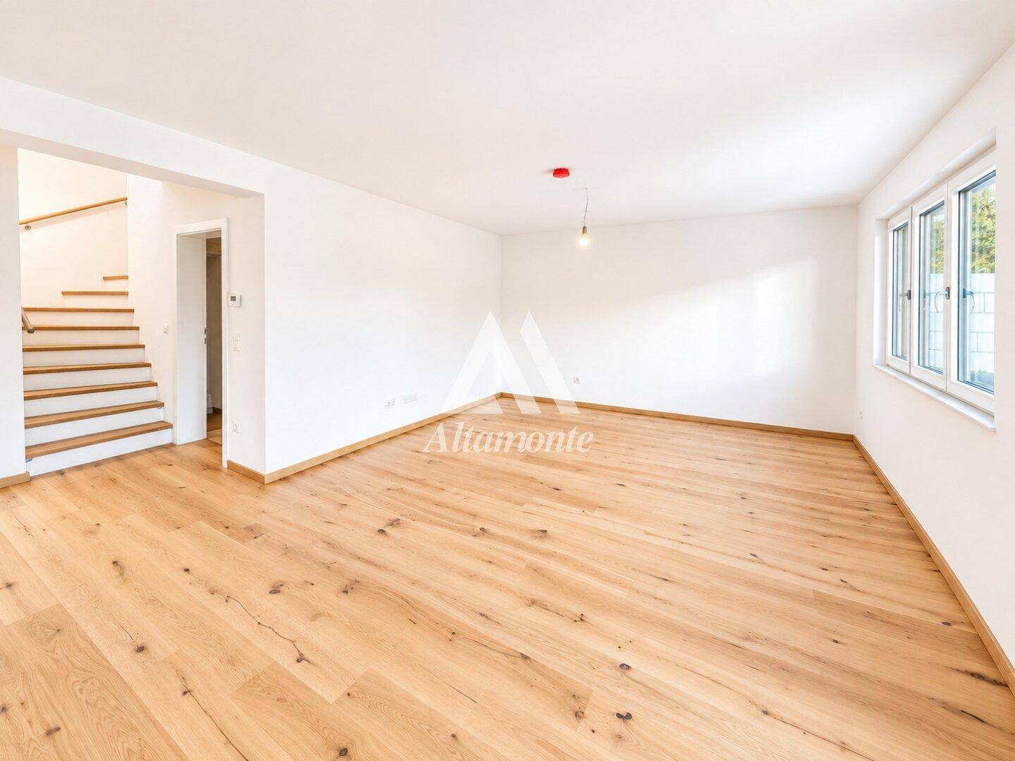 Geräumiges Wohnzimmer mit hellem Holzboden und Treppenaufgang in einem Neubau.