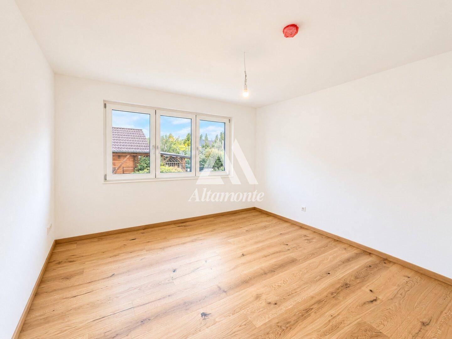 Ruhiges Schlafzimmer mit Holzboden und Blick ins Grüne durch das Fenster.