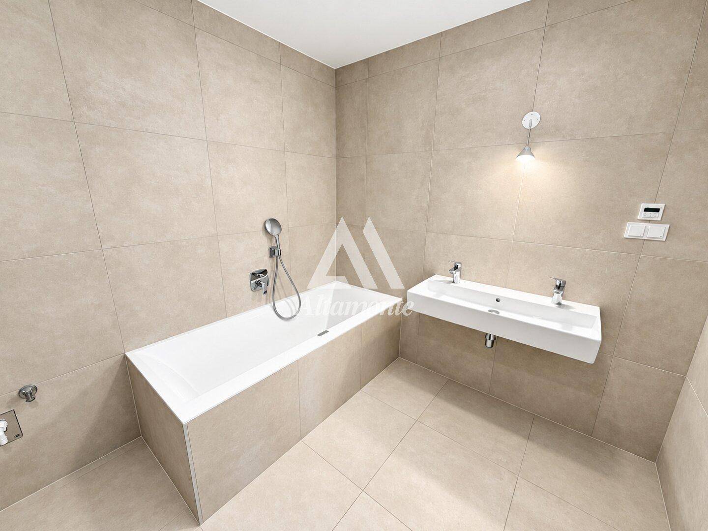 Modernes Badezimmer mit beigefarbenen Fliesen, einer Badewanne und einem Doppelwaschbecken.