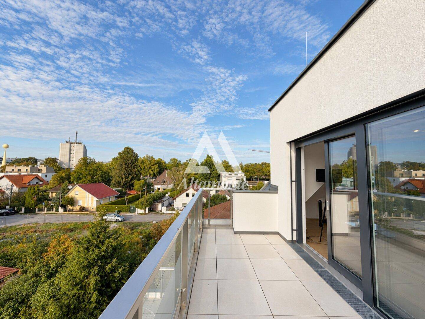 Geräumiger Balkon mit Glasgeländer und weitem Blick über die Umgebung und die Stadt.