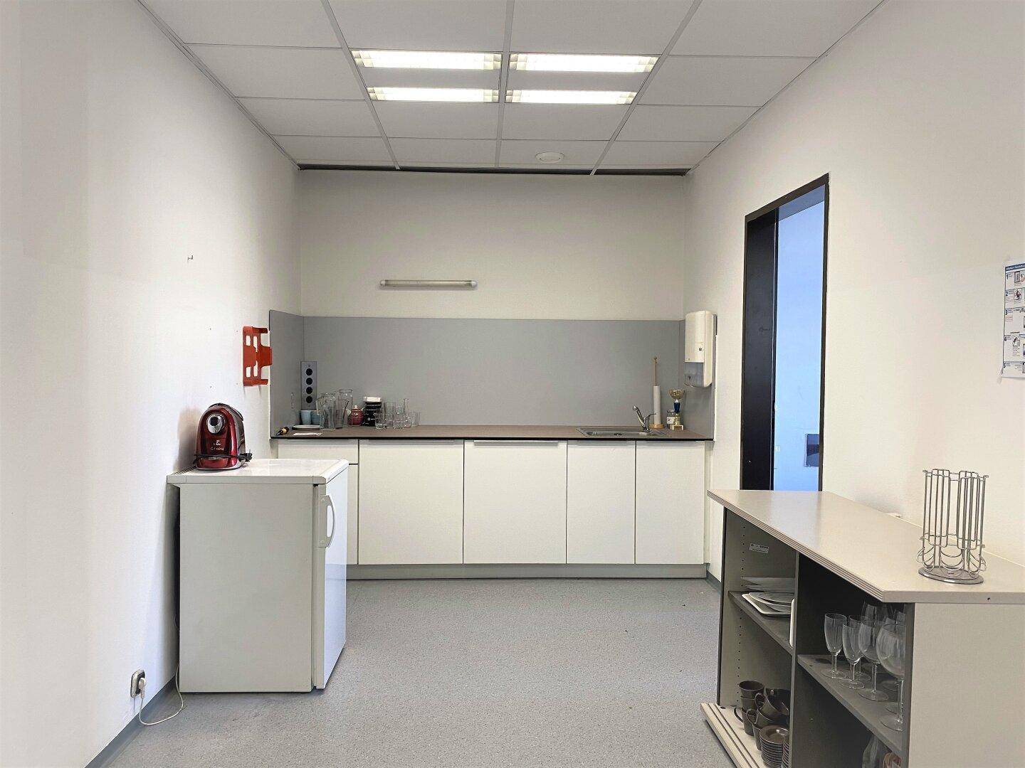 Funktionale Teeküche mit weißen Schränken, Spüle, Kühlschrank und Kaffeemaschine für Mitarbeiter.
