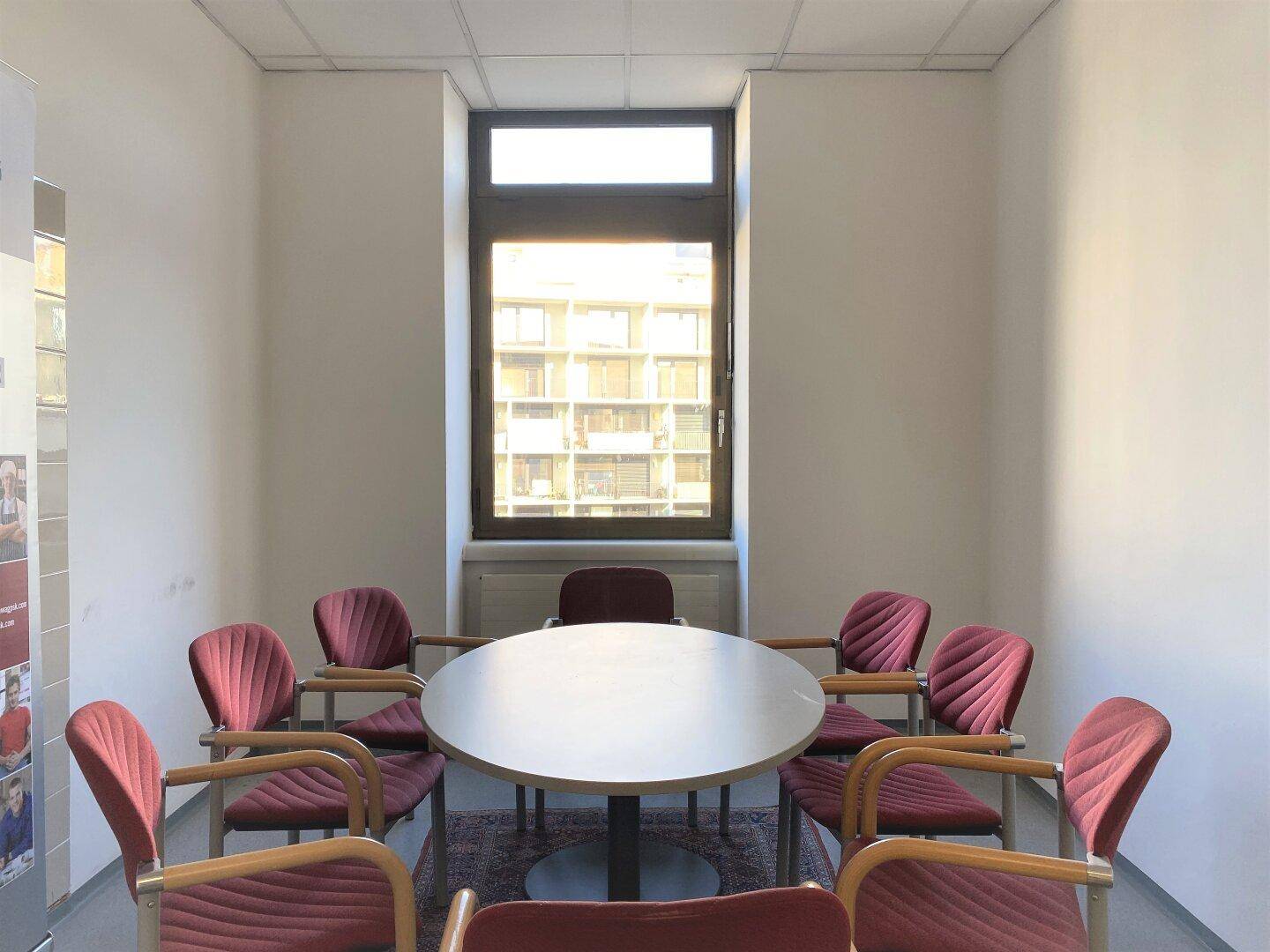 Besprechungsraum mit rundem Tisch und roten Stühlen, ideal für kleine Arbeitsgruppen oder Diskussionen.