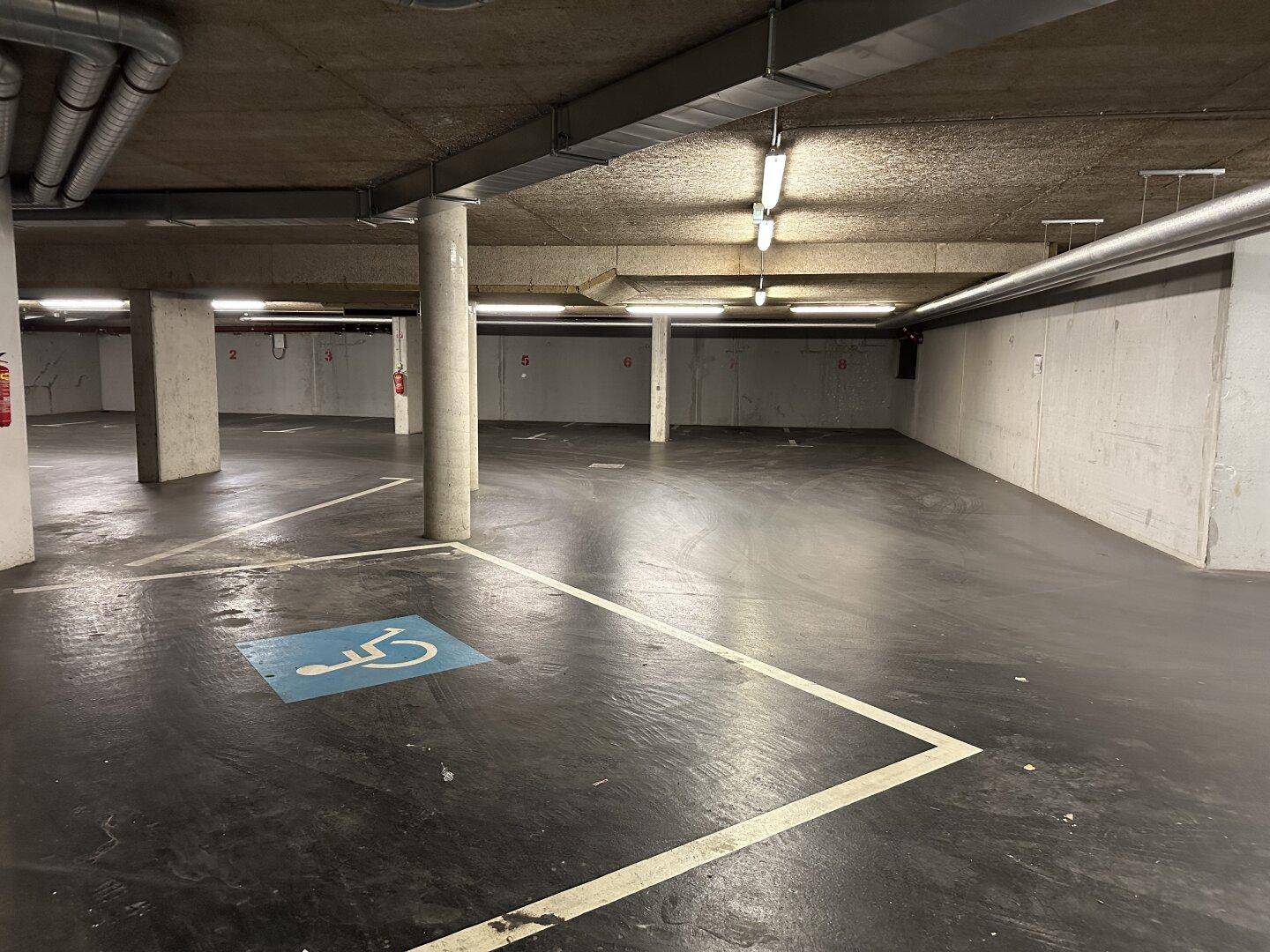 Geräumige Tiefgarage mit markierten Parkplätzen und Säulen, inklusive Behindertenparkplatz.