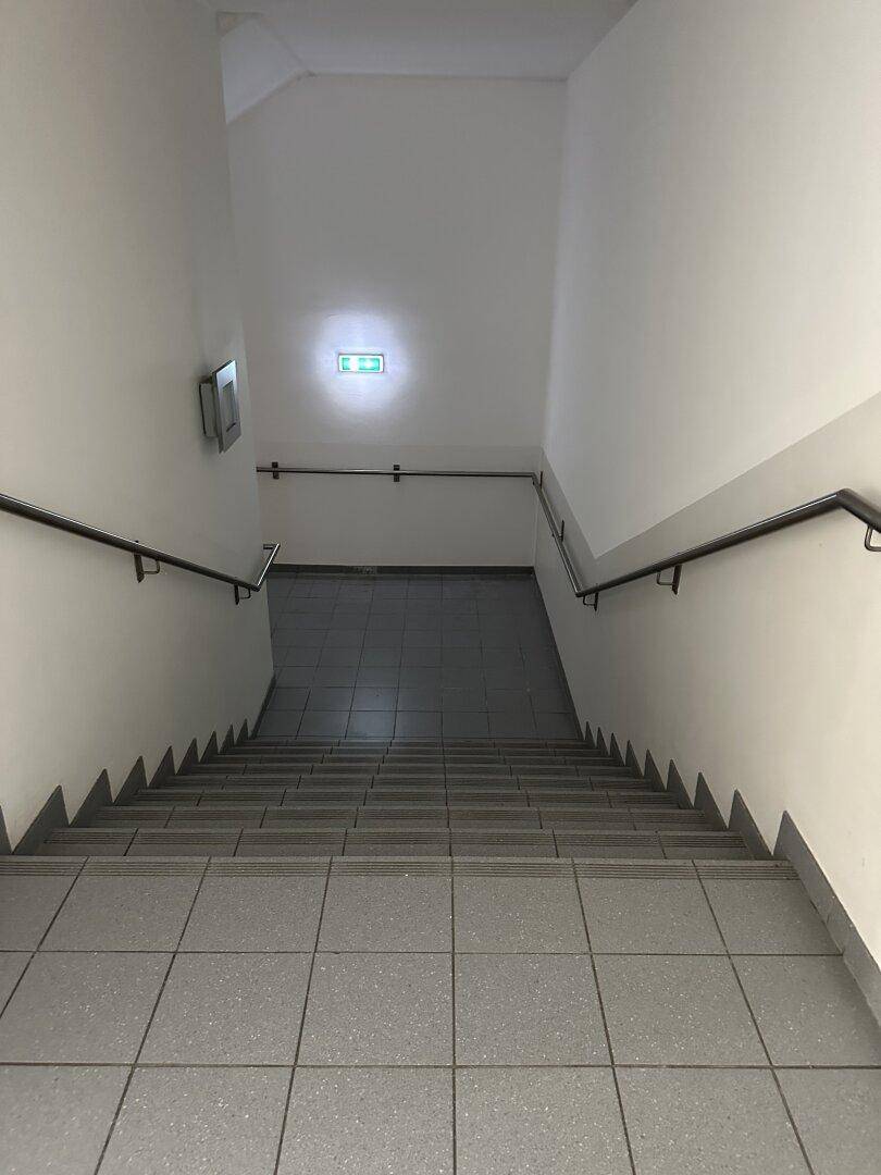 Treppenhaus mit grauen Fliesenstufen und Handläufen, das zu den oberen Etagen führt.