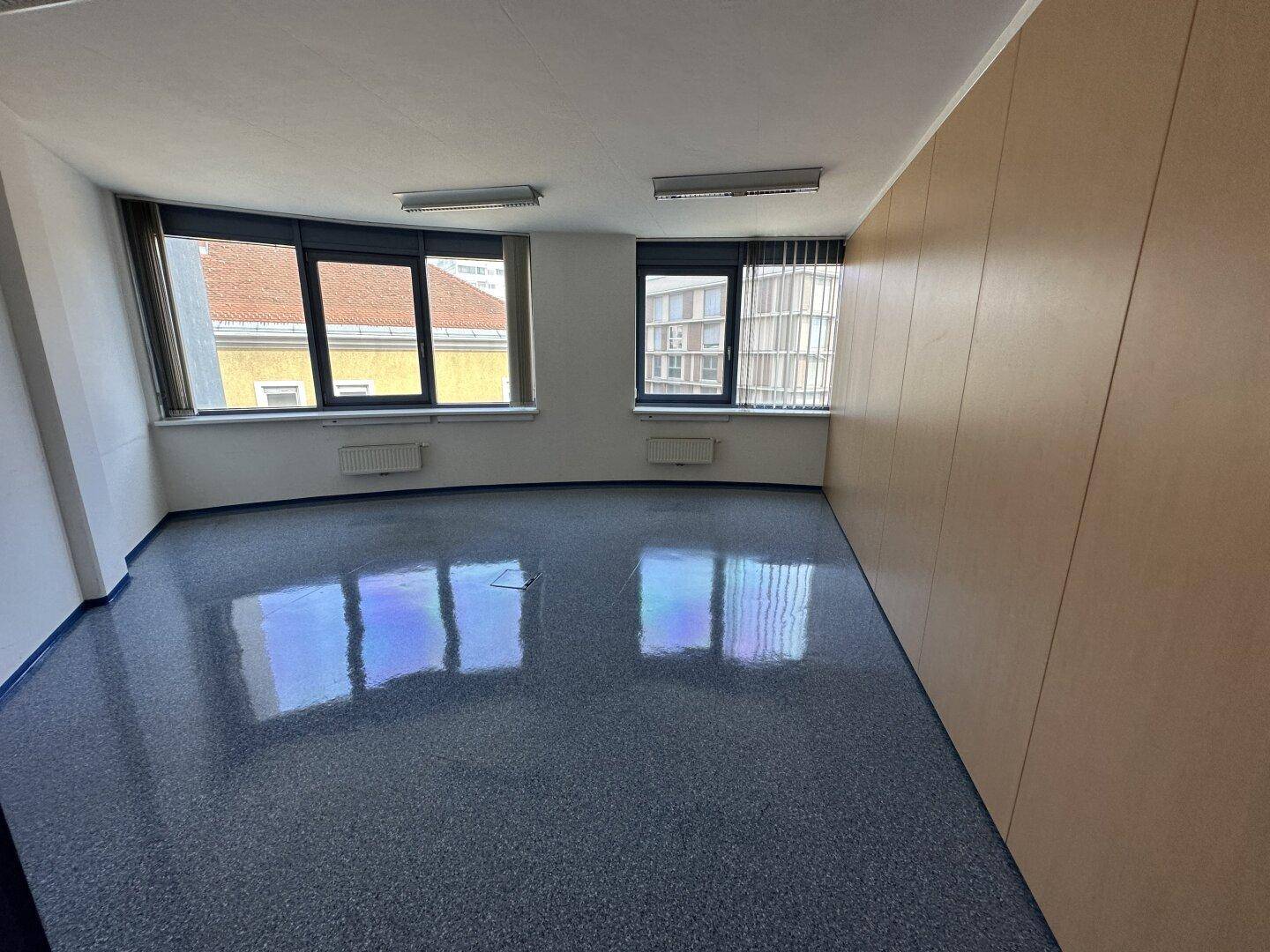 Heller Büroraum mit blauen Vinylböden und großen Fenstern, die einen Blick auf die Umgebung bieten.