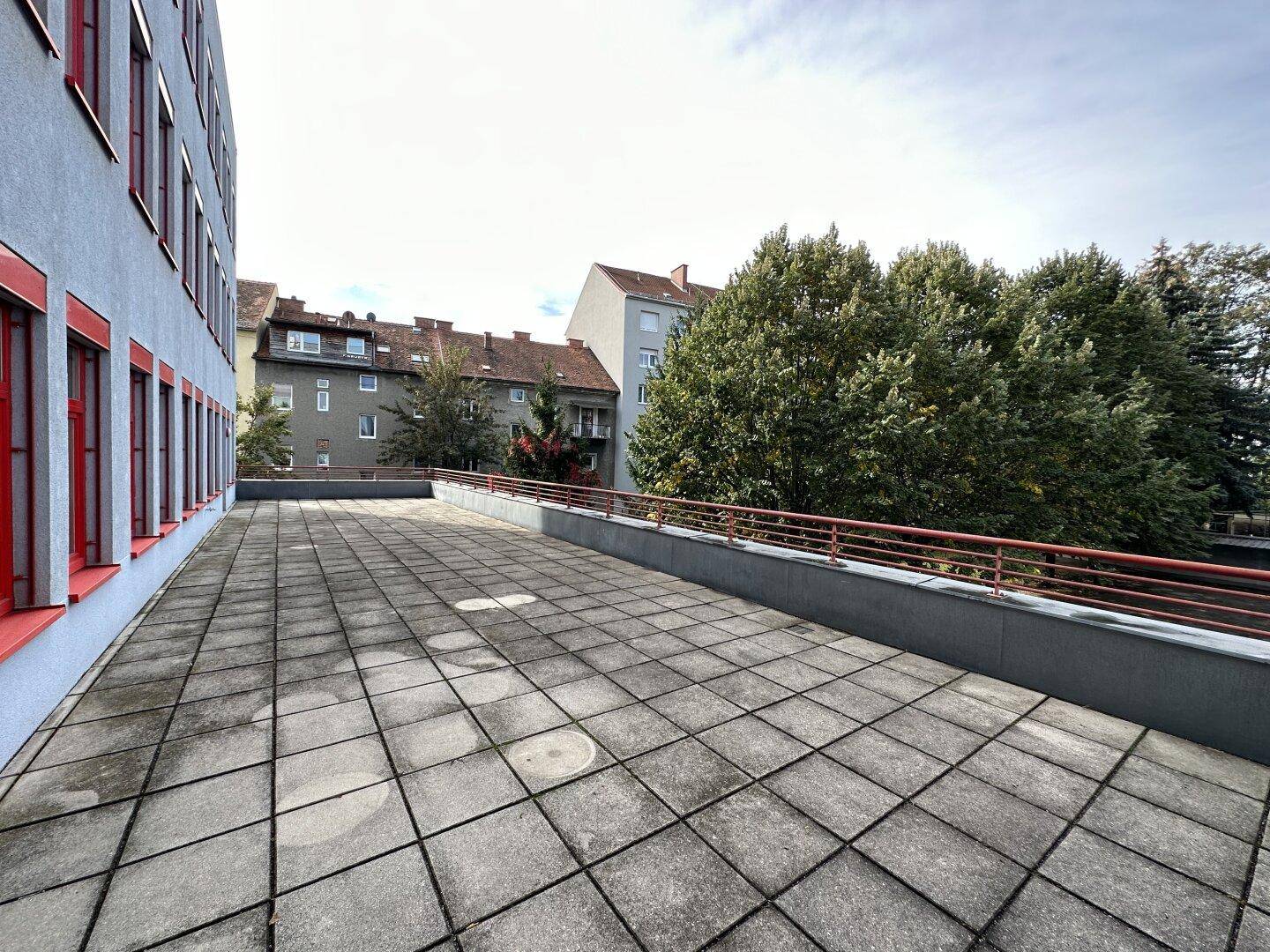 Große gepflasterte Terrasse mit Geländer und Blick auf die umliegenden Gebäude und Bäume.