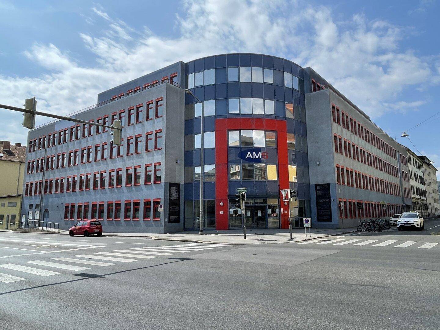 Modernes Bürogebäude an einer Straßenecke mit großer Glasfassade und blauen sowie roten Akzenten.