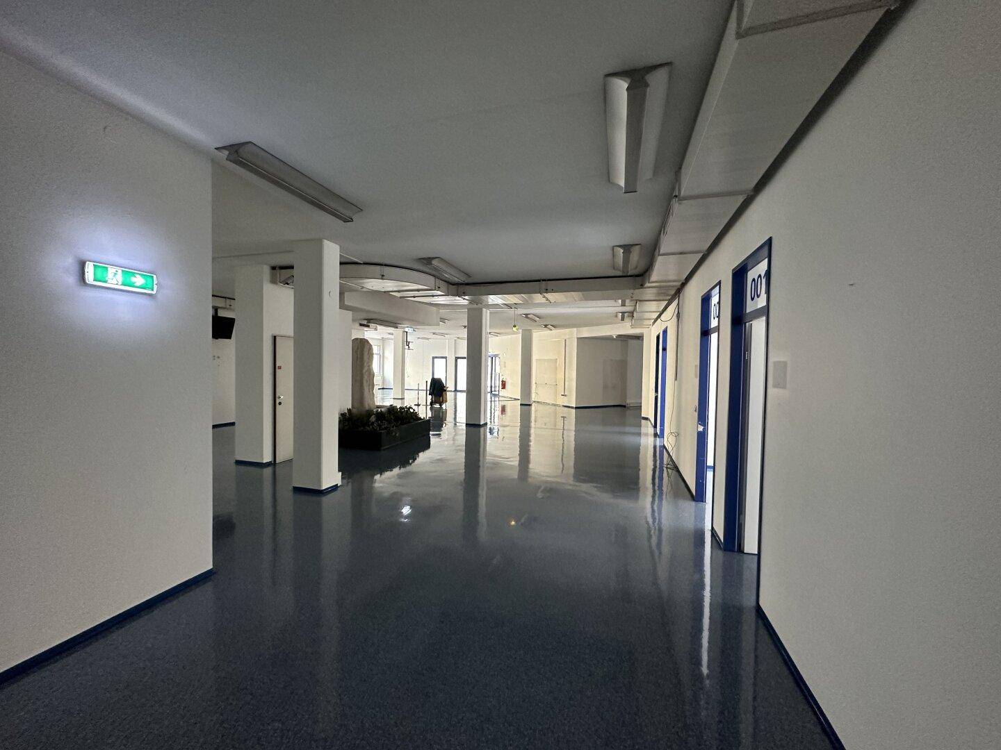 Langer Flur mit glänzendem blauen Boden und Türen, der zu verschiedenen Büroräumen führt.