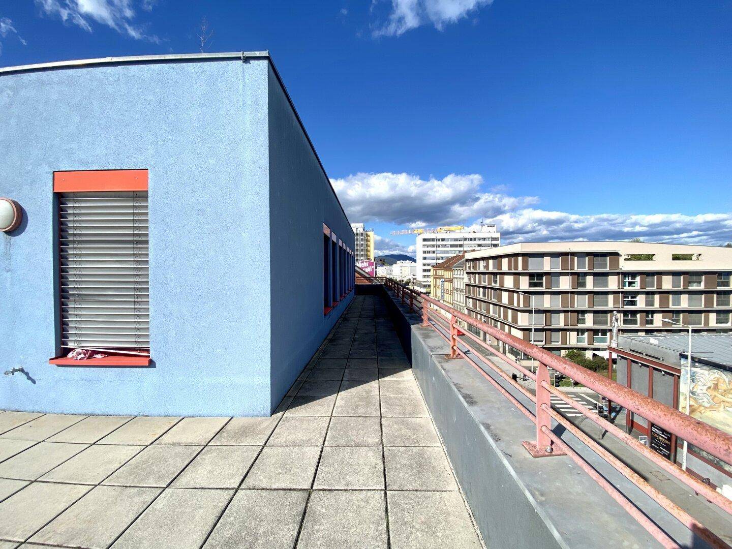 Langer, gepflasterter Weg auf dem Dach mit Geländer und Blick auf die umliegenden Gebäude.