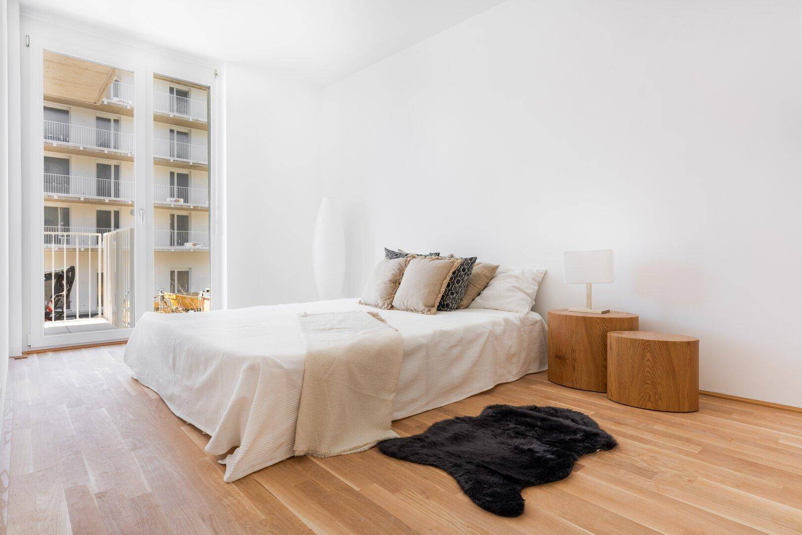 Helles Schlafzimmer mit Holzboden, minimalistischer Einrichtung und Balkonzugang.