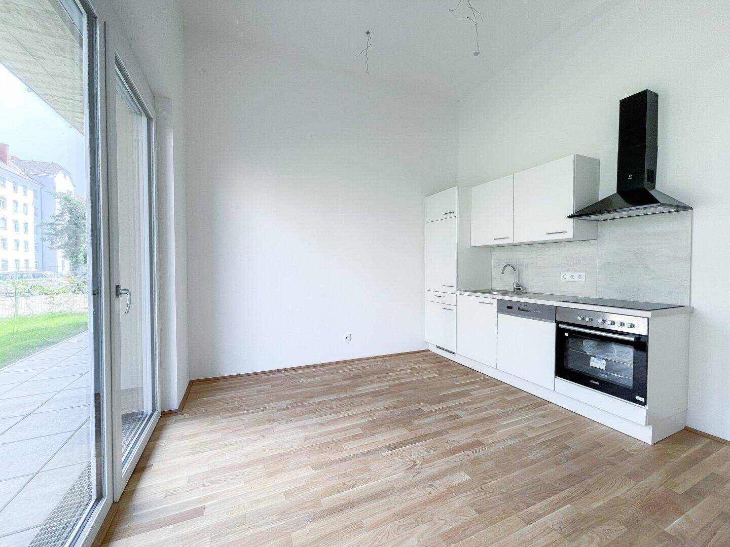 Moderne Einbauküche in hellem Raum mit Zugang zu einer Terrasse und Holzparkettboden.