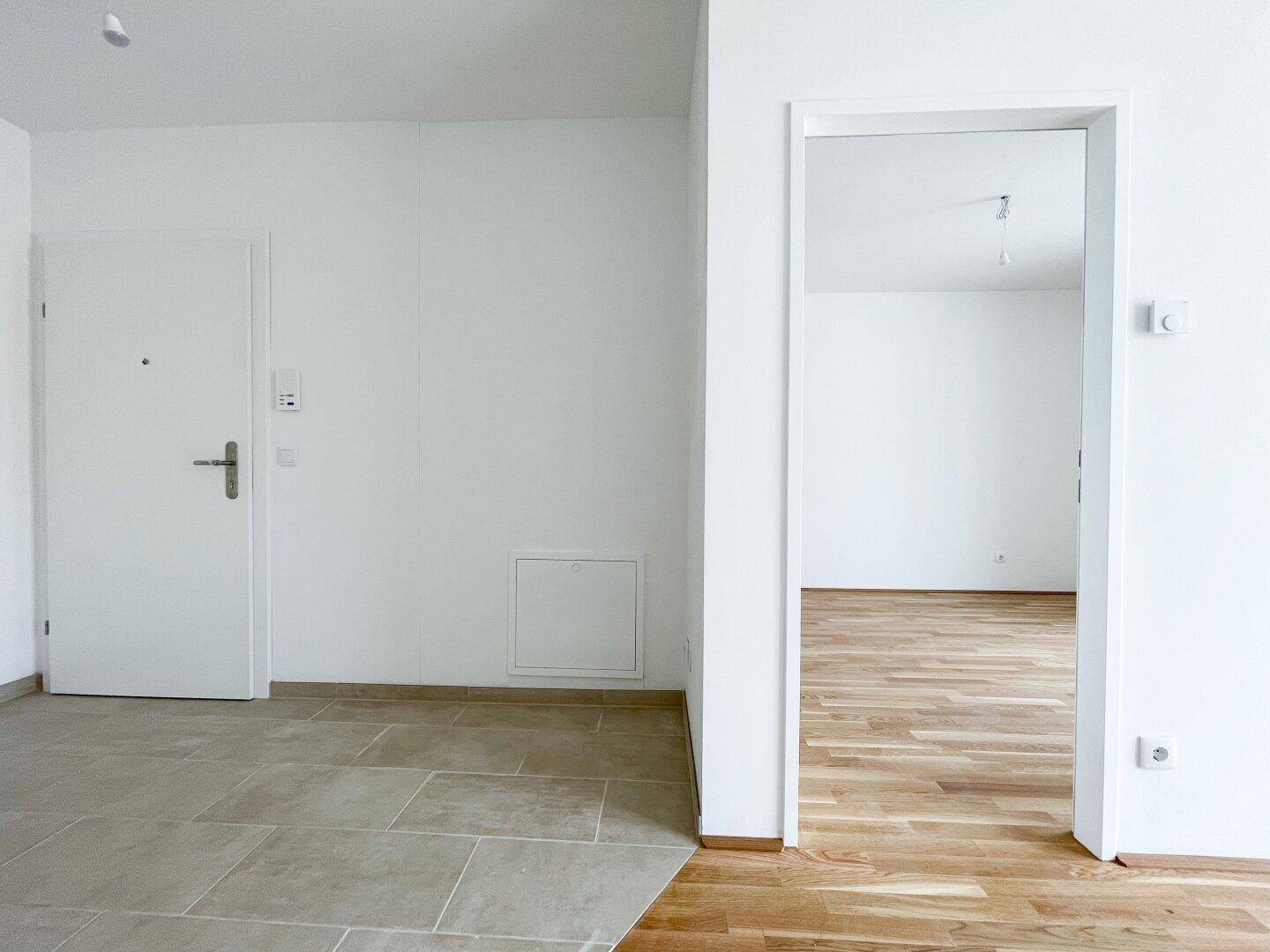 Eingangsbereich mit Fliesenboden, der in einen hellen Raum mit Holzboden übergeht.