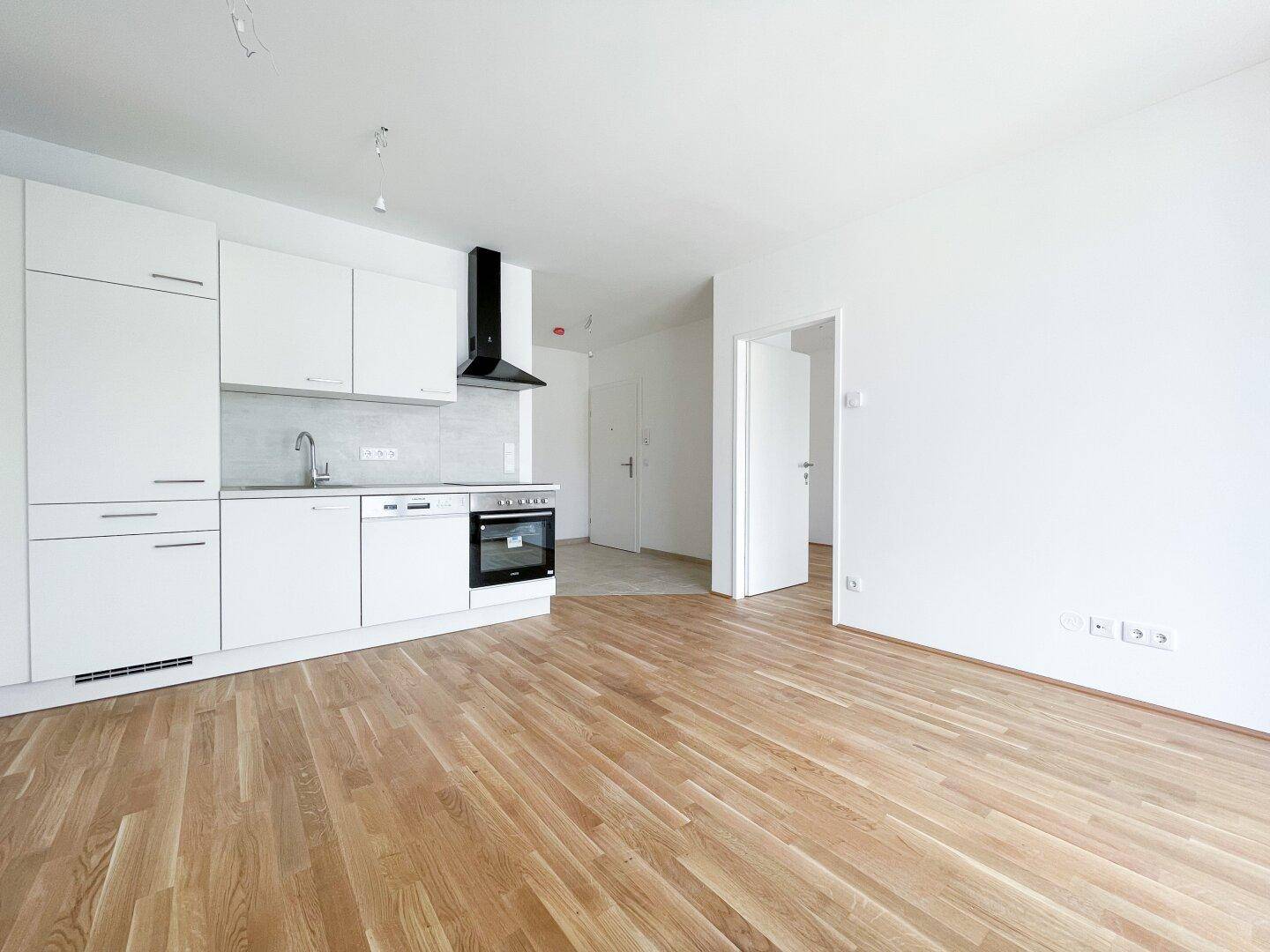 Moderne, weiße Einbauküche mit Kochfeld, Backofen und Dunstabzugshaube in einem hellen Raum.