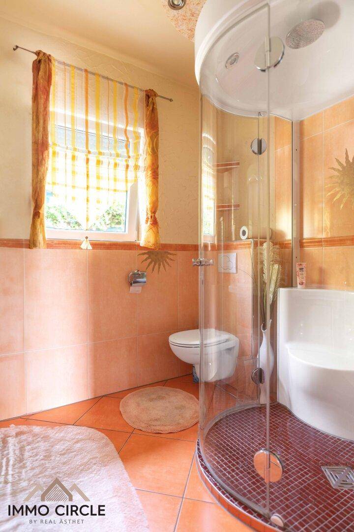 Badezimmer mit Duschkabine, WC, Fenster und orangefarbenen Fliesen.