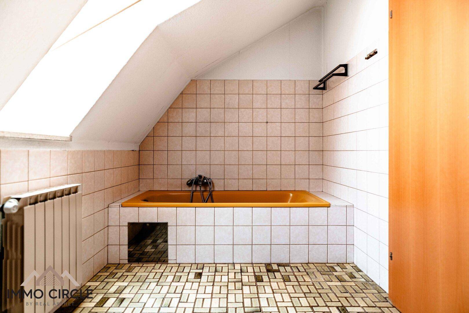 Badezimmer im Dachgeschoss mit Badewanne, Fliesen und Dachschräge.
