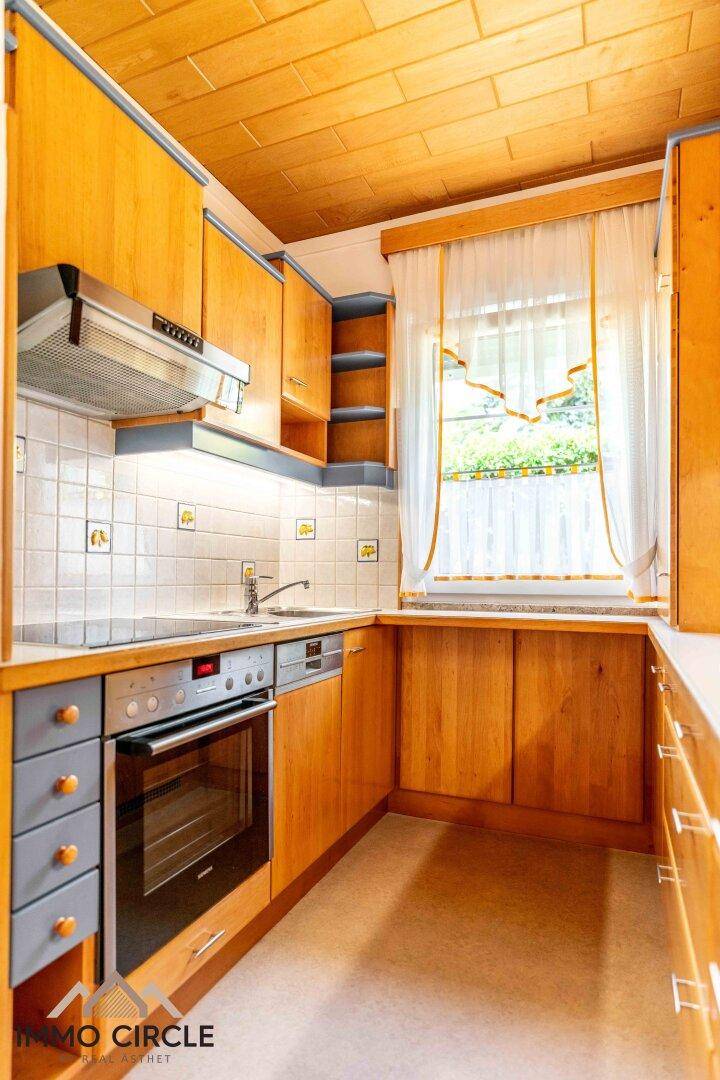 Funktionale Holzküche mit Einbaugeräten, Fliesenrückwand und Fenster.