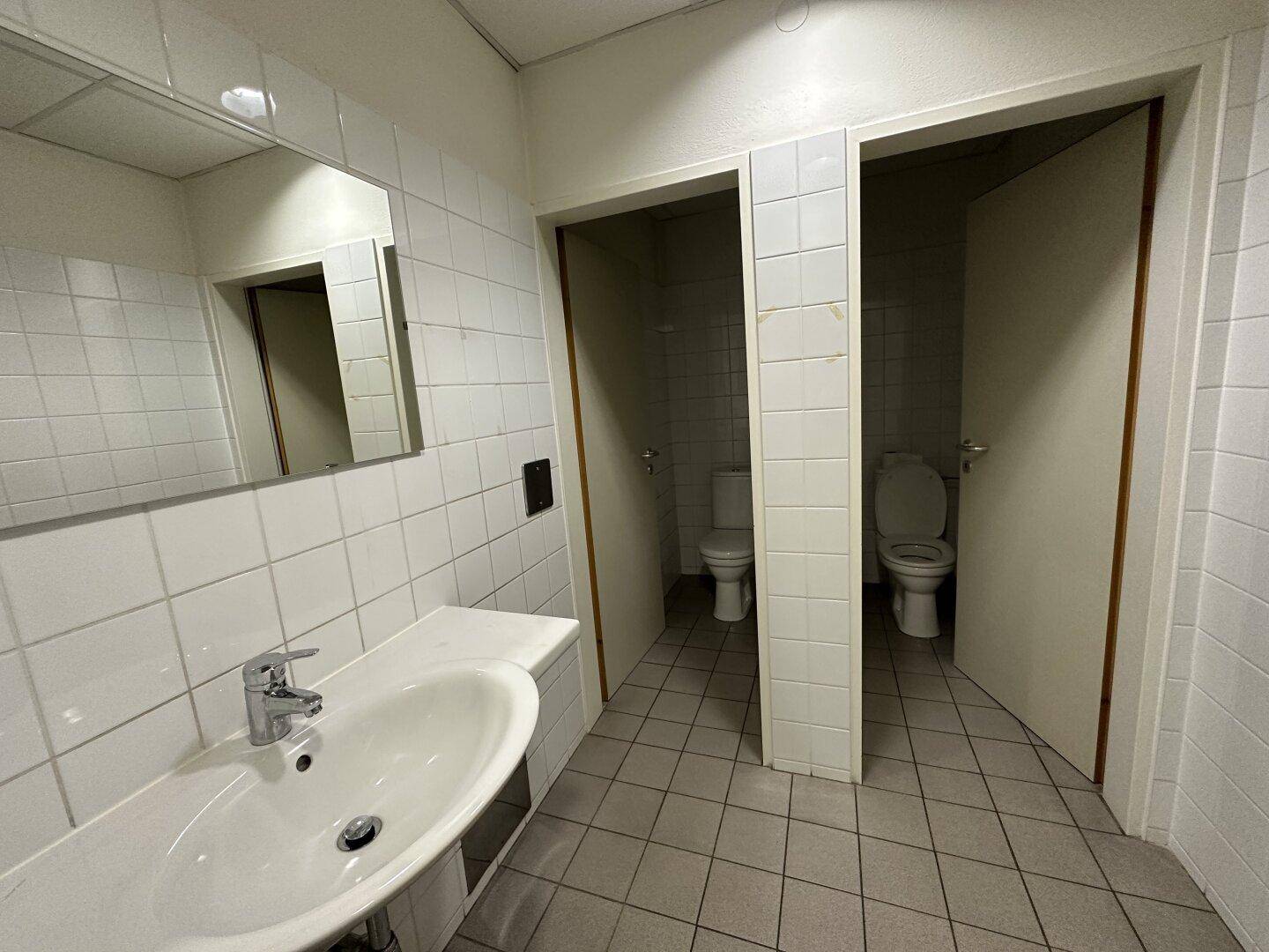 Gefliester Sanitärbereich mit Waschbecken und mehreren Toilettenkabinen, sauber und funktional.