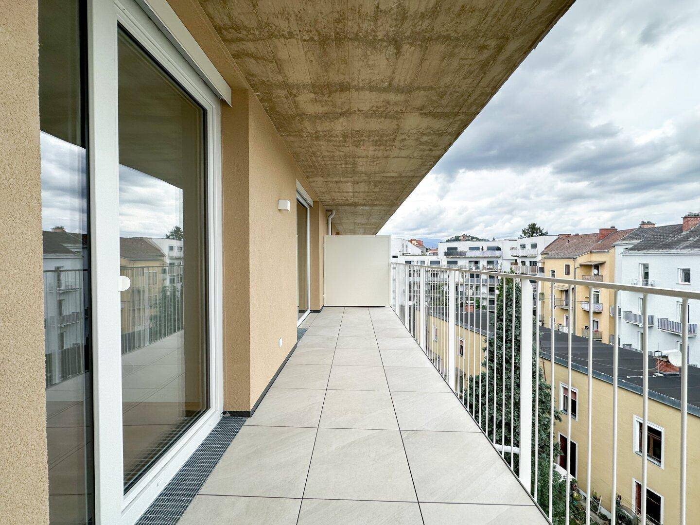 Langer Balkon mit modernem Fliesenboden und weitem Blick über die städtische Umgebung.