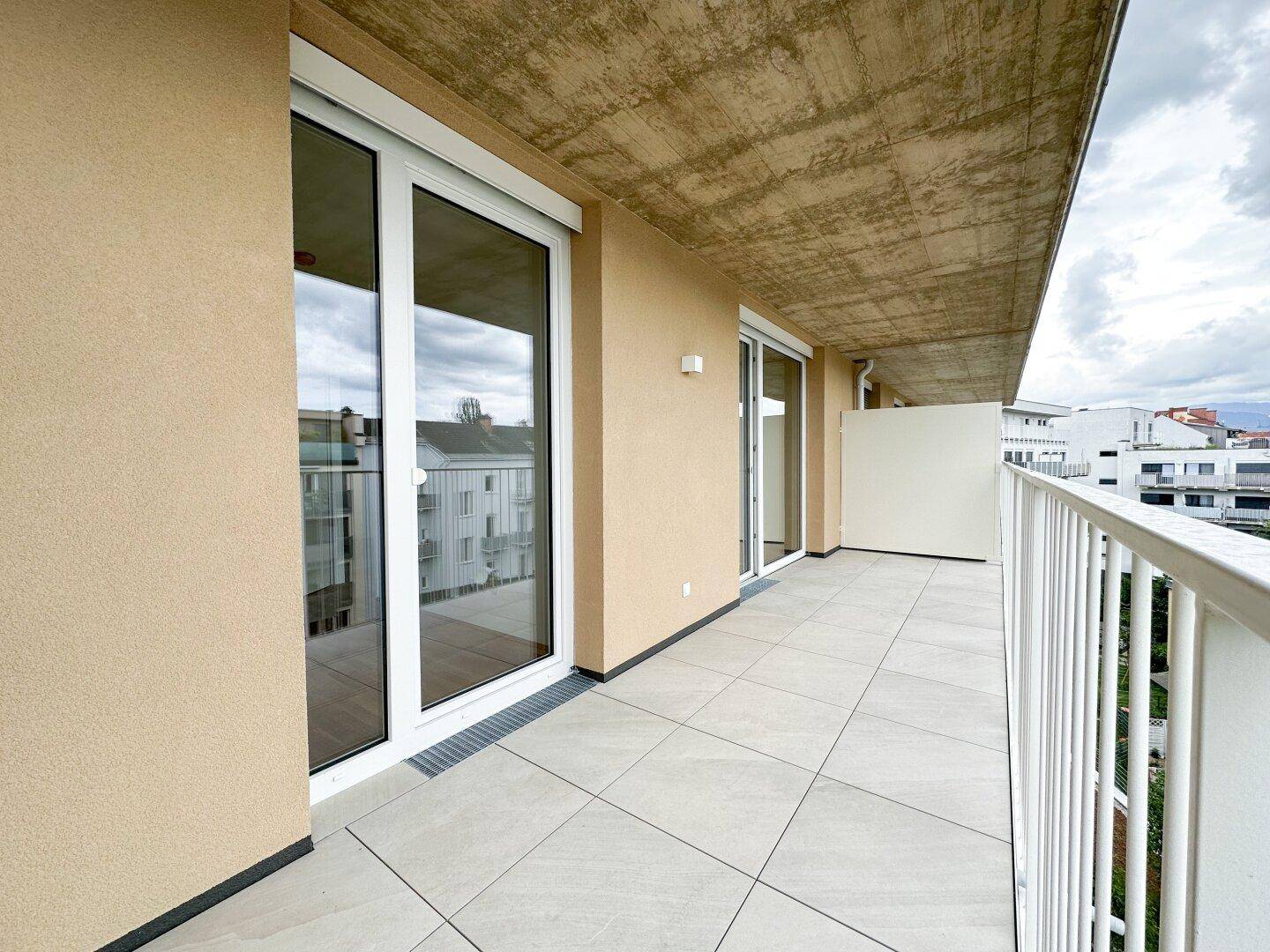 Geräumiger Balkon mit Fliesenboden, weißem Geländer und Blick auf die umliegenden Gebäude.