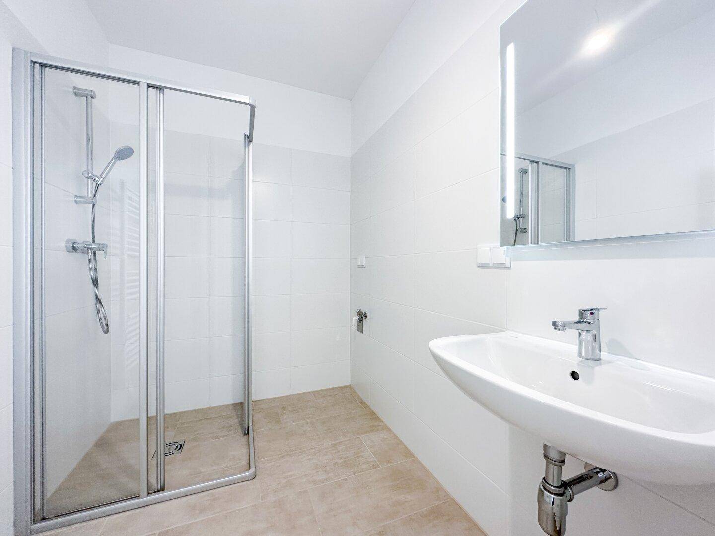 Modernes Badezimmer mit Duschkabine, Einzelwaschbecken und hellen Fliesen an Wänden und Boden.
