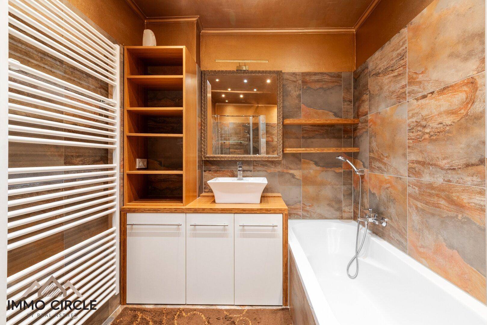 Badezimmer mit Badewanne, modernem Waschbecken, Holzregalen und gemusterten Fliesen.