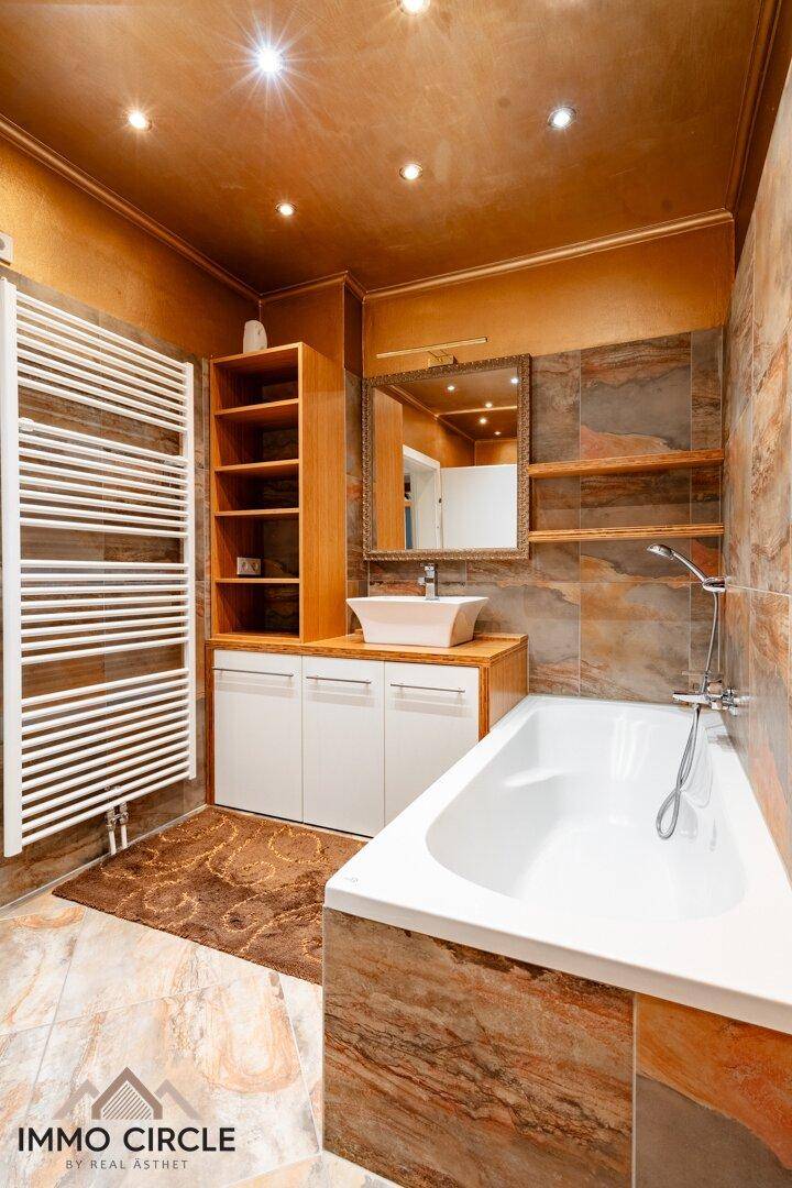 Badezimmer mit Badewanne, Aufsatzwaschbecken, Holzmöbeln und Heizkörper für Handtücher.