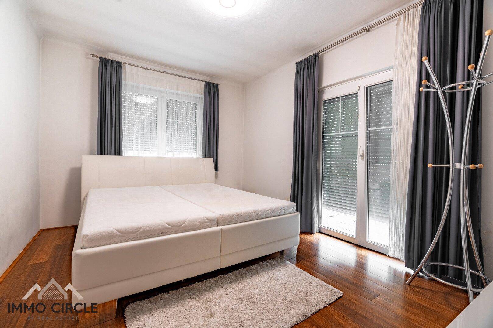 Schlafzimmer mit Doppelbett, dunklen Vorhängen und Zugang zu einem Außenbereich.