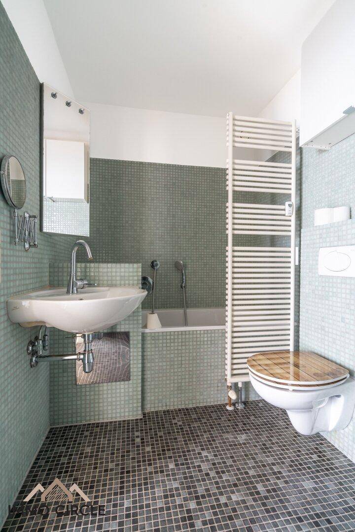 Badezimmer mit Mosaikfliesen, Badewanne, Waschbecken und beheiztem Handtuchhalter.