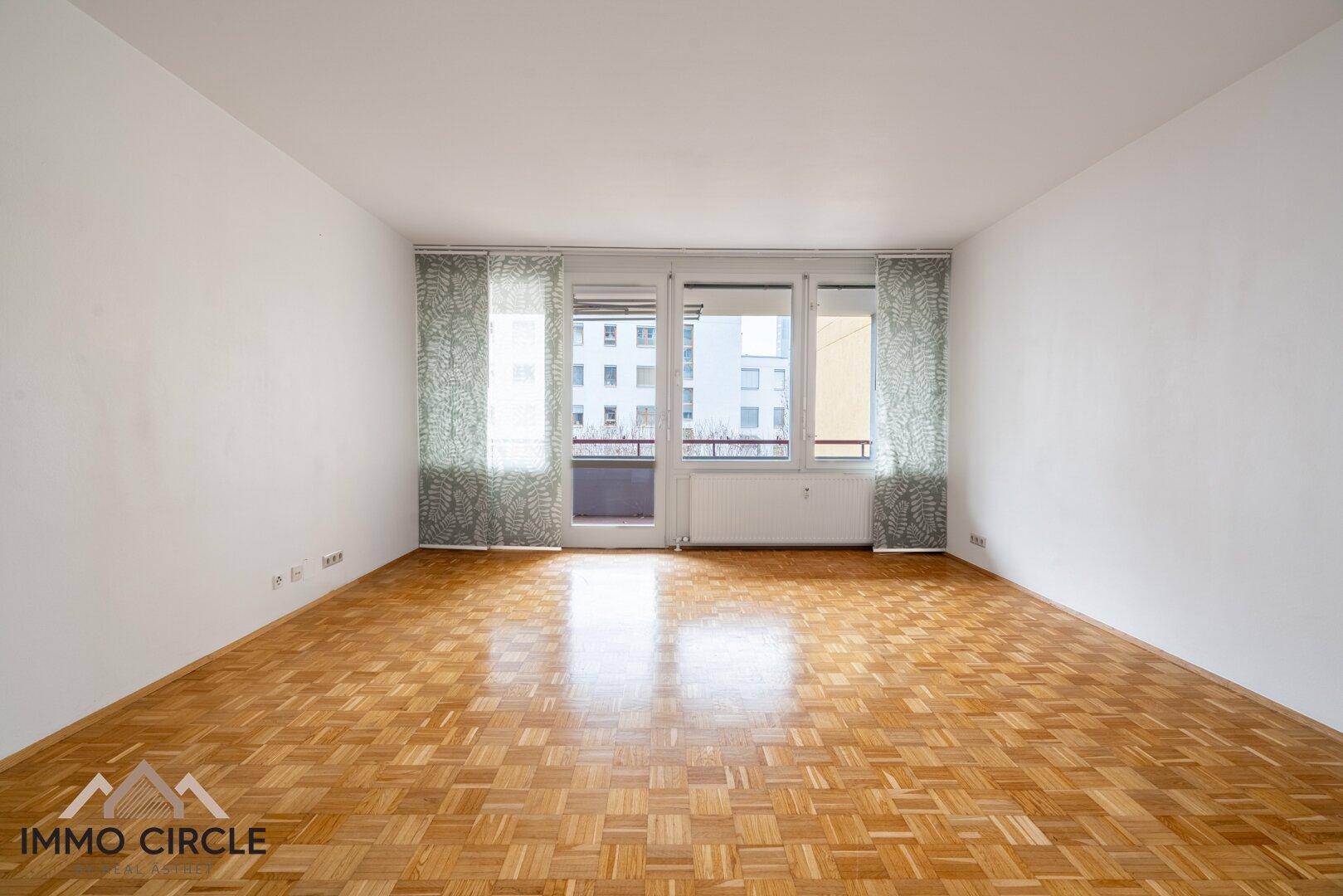 Lichtdurchflutetes Wohnzimmer mit Parkettboden und großen Fenstern zum Außenbereich.