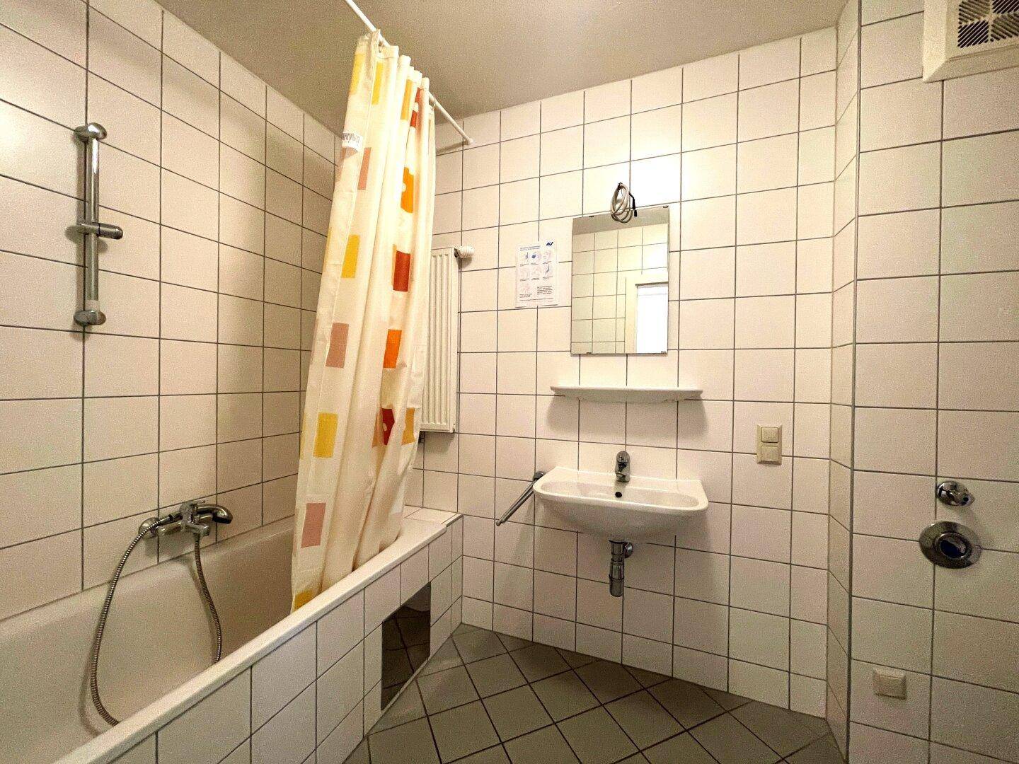 Funktionales Badezimmer mit Badewanne, Duschvorhang und weißen Fliesen an Wänden und Boden.