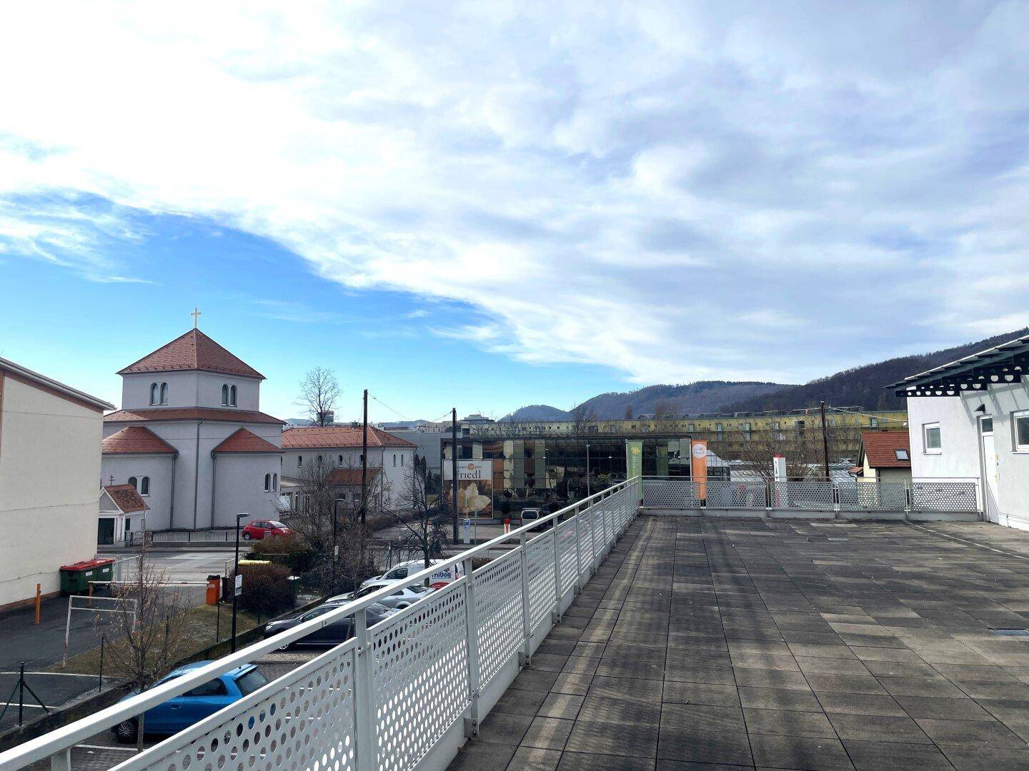 Weitläufige Dachfläche mit Blick auf die umliegende Stadt und die Berge im Hintergrund unter blauem Himmel.