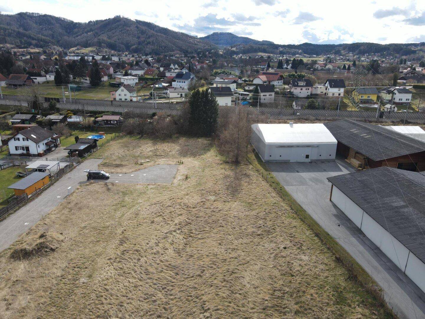 Überblick aus der Vogelperspektive über ein Grundstücksareal mit angrenzenden Gebäuden und Bergpanorama.