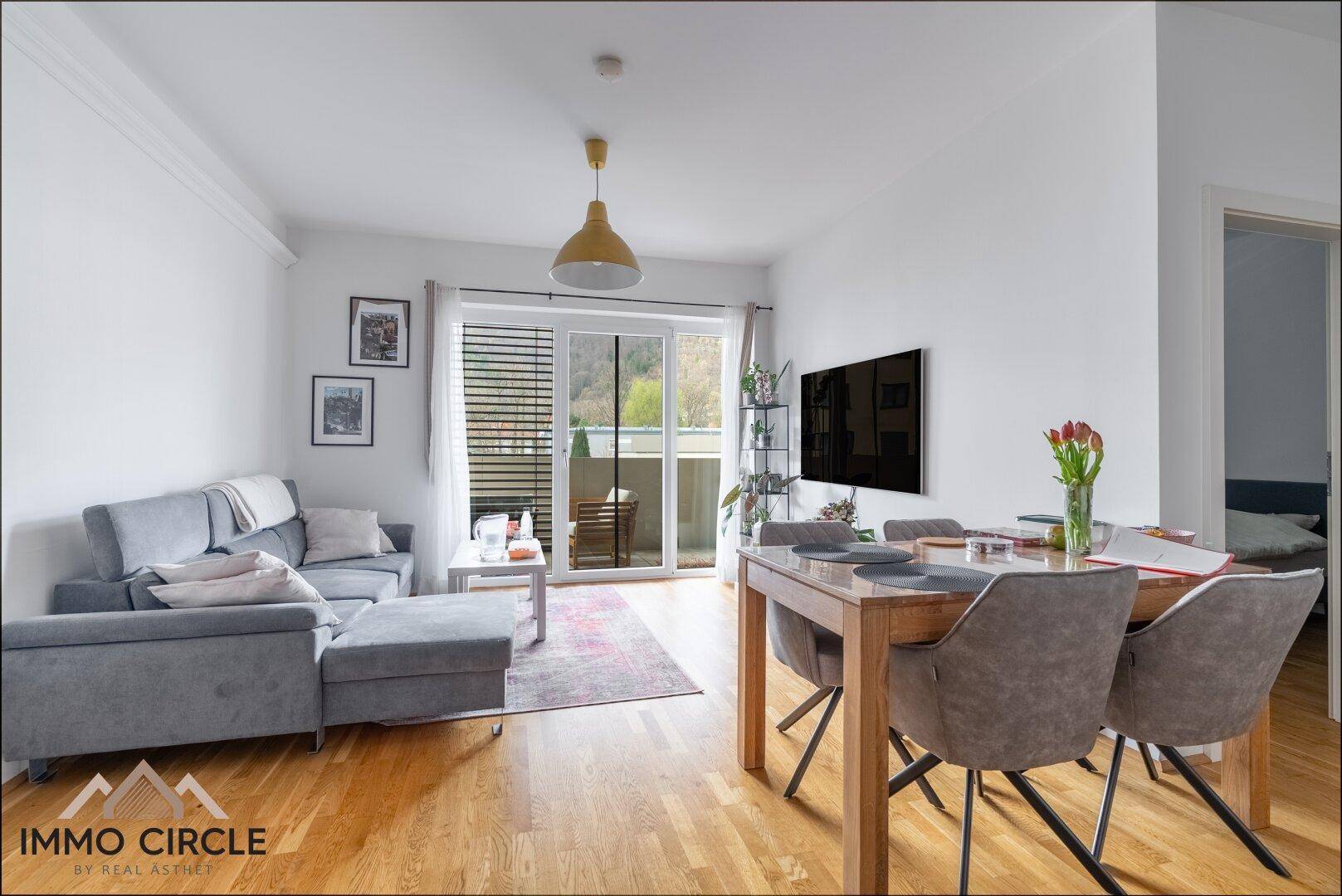 Heller Wohn- und Essbereich mit Parkettboden, bequemer Couch und Zugang zum Balkon.