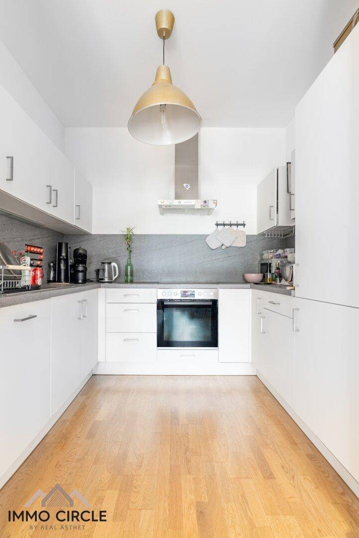 Moderne, helle Küche mit weißen Schränken, Holzboden und integrierten Geräten.