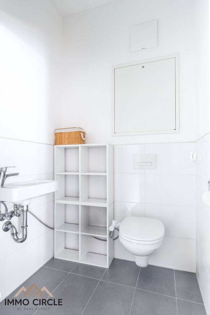 Kleines Gäste-WC mit Wand-WC, Waschbecken und grauen Bodenfliesen.