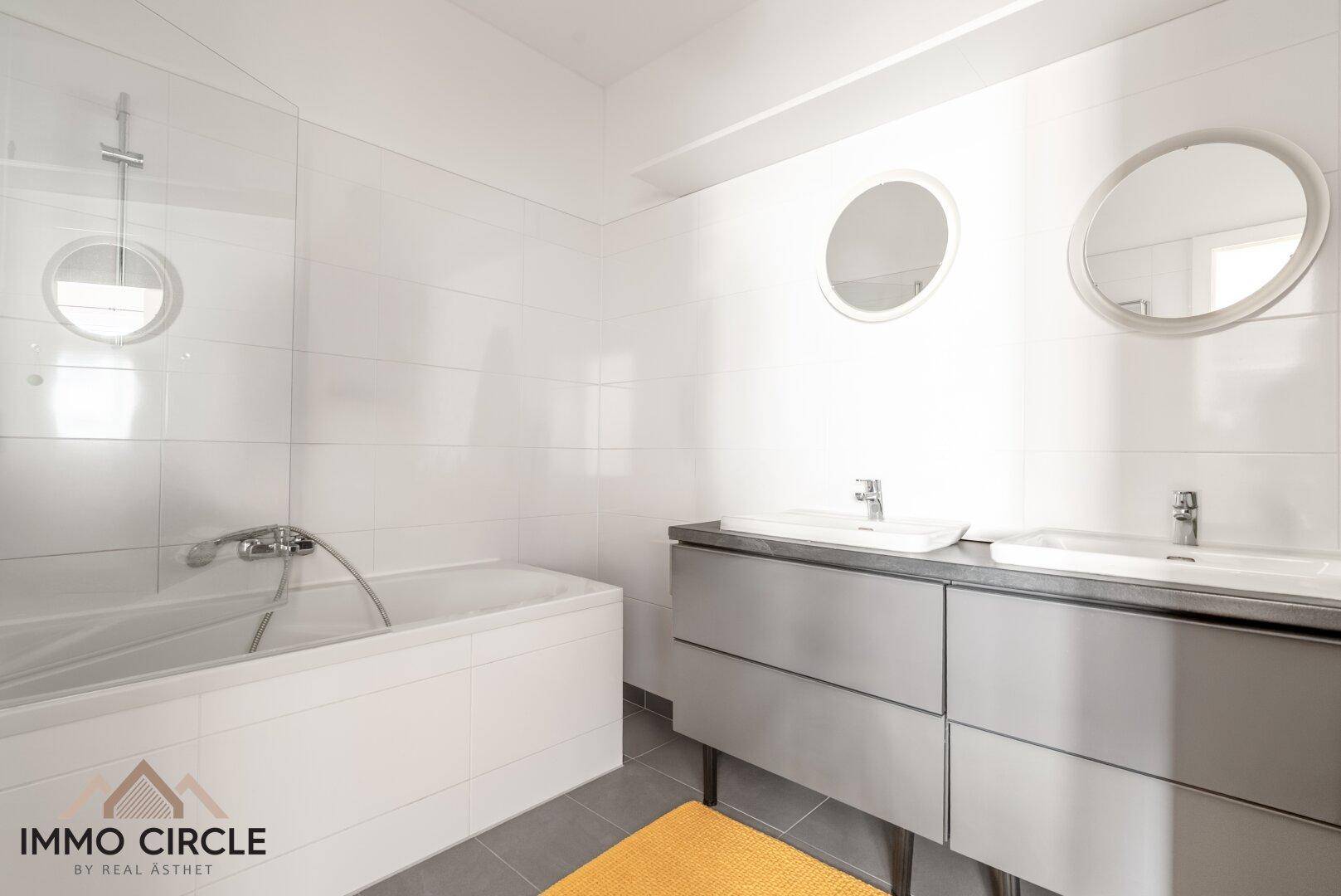 Modernes Badezimmer mit Doppelwaschbecken, Badewanne und Dusche, hell gefliest.