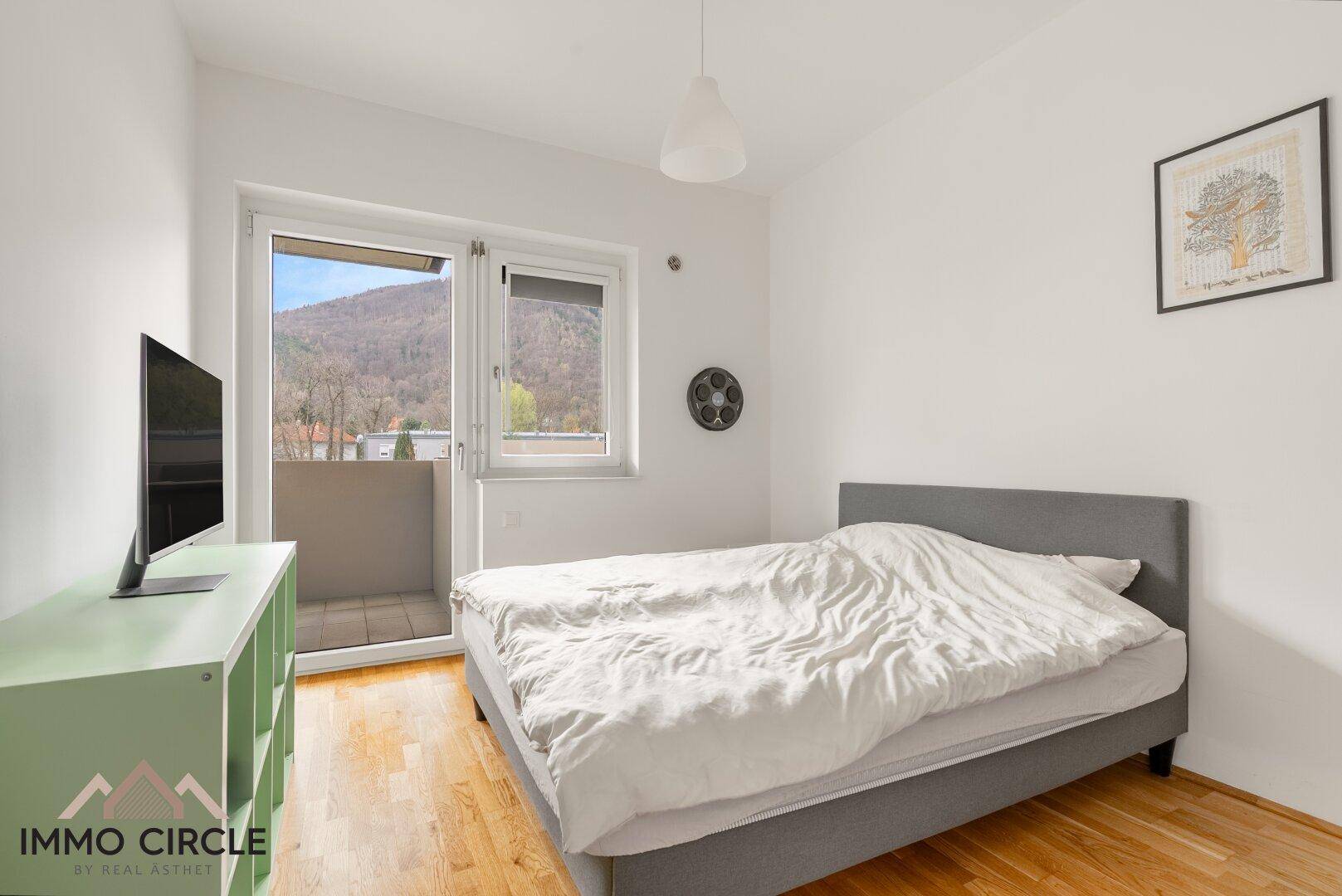 Schlafzimmer mit Doppelbett, Parkettboden und Zugang zu einem kleinen Balkon mit Bergblick.