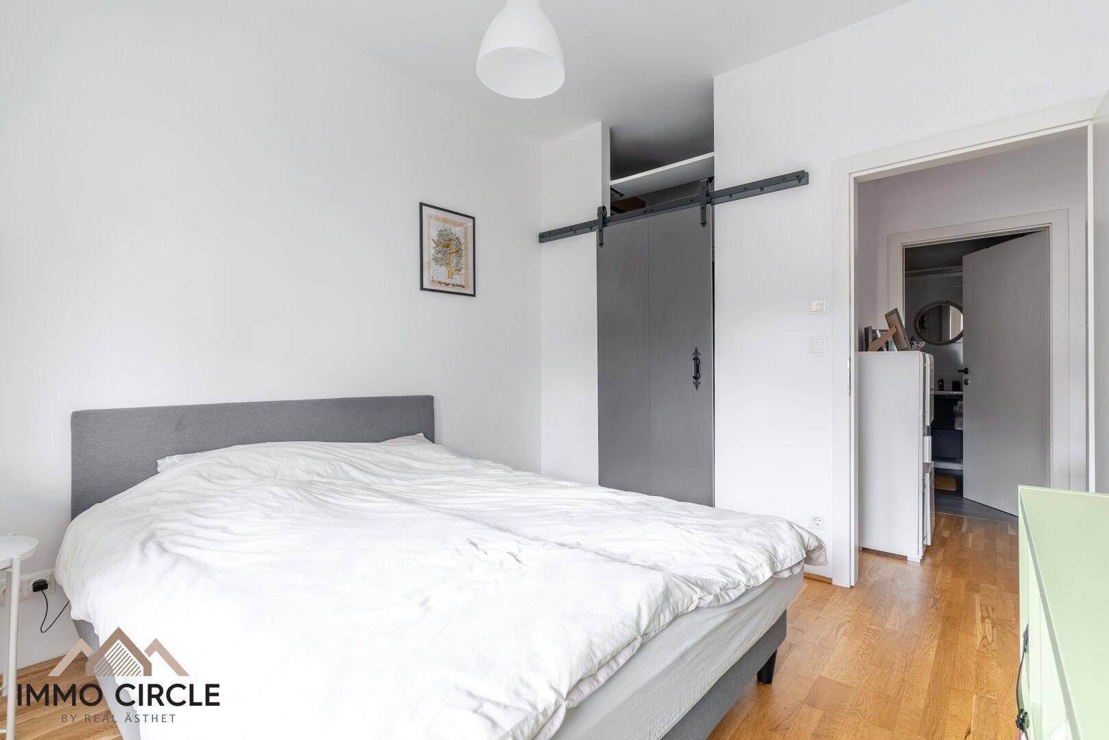 Schlafzimmer mit Doppelbett, Parkettboden und Schiebetür zu einem angrenzenden Bereich.