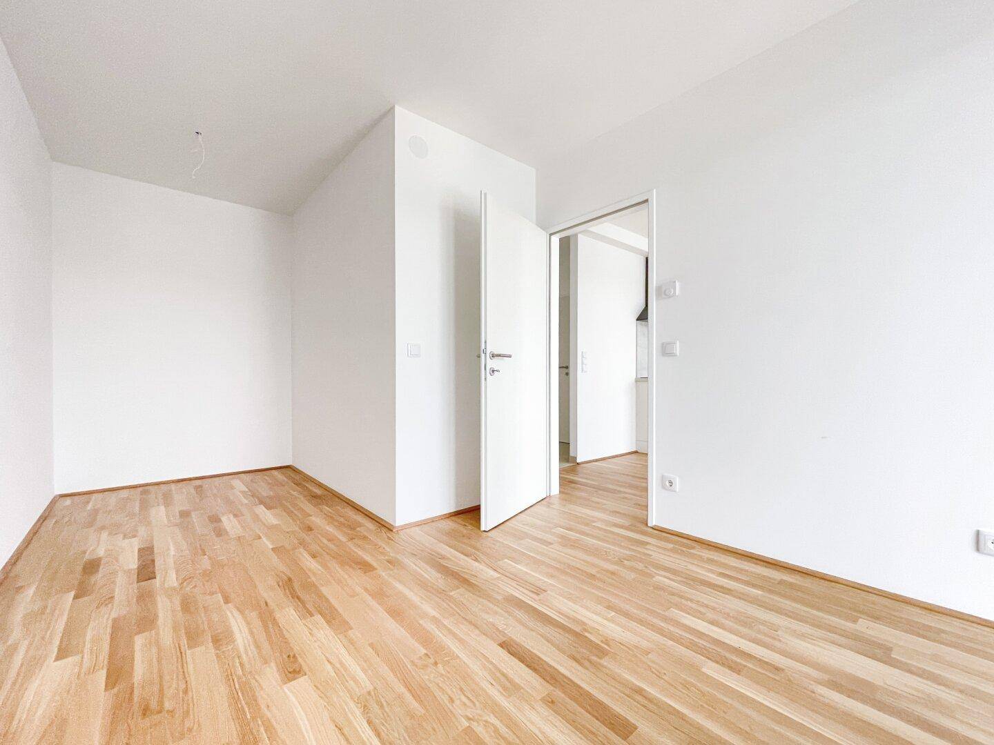Leeres Zimmer mit hellem Holzboden und weißen Wänden, bereit zur individuellen Gestaltung.