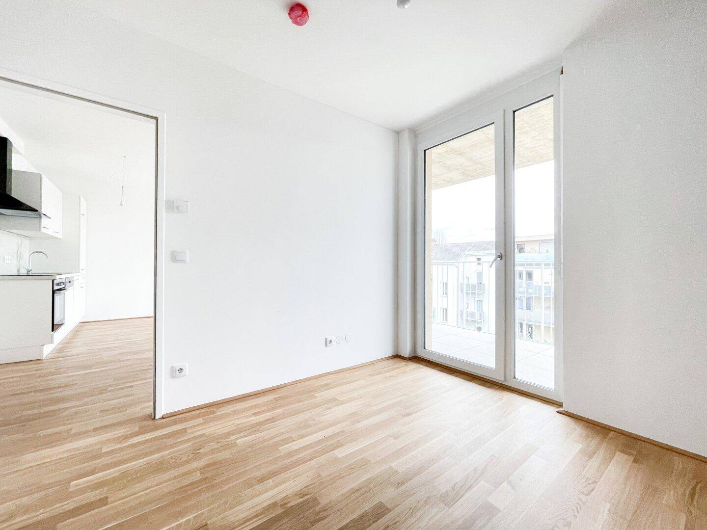 Helles Zimmer mit Holzboden und großem Fenster, das Zugang zu einem Balkon bietet.
