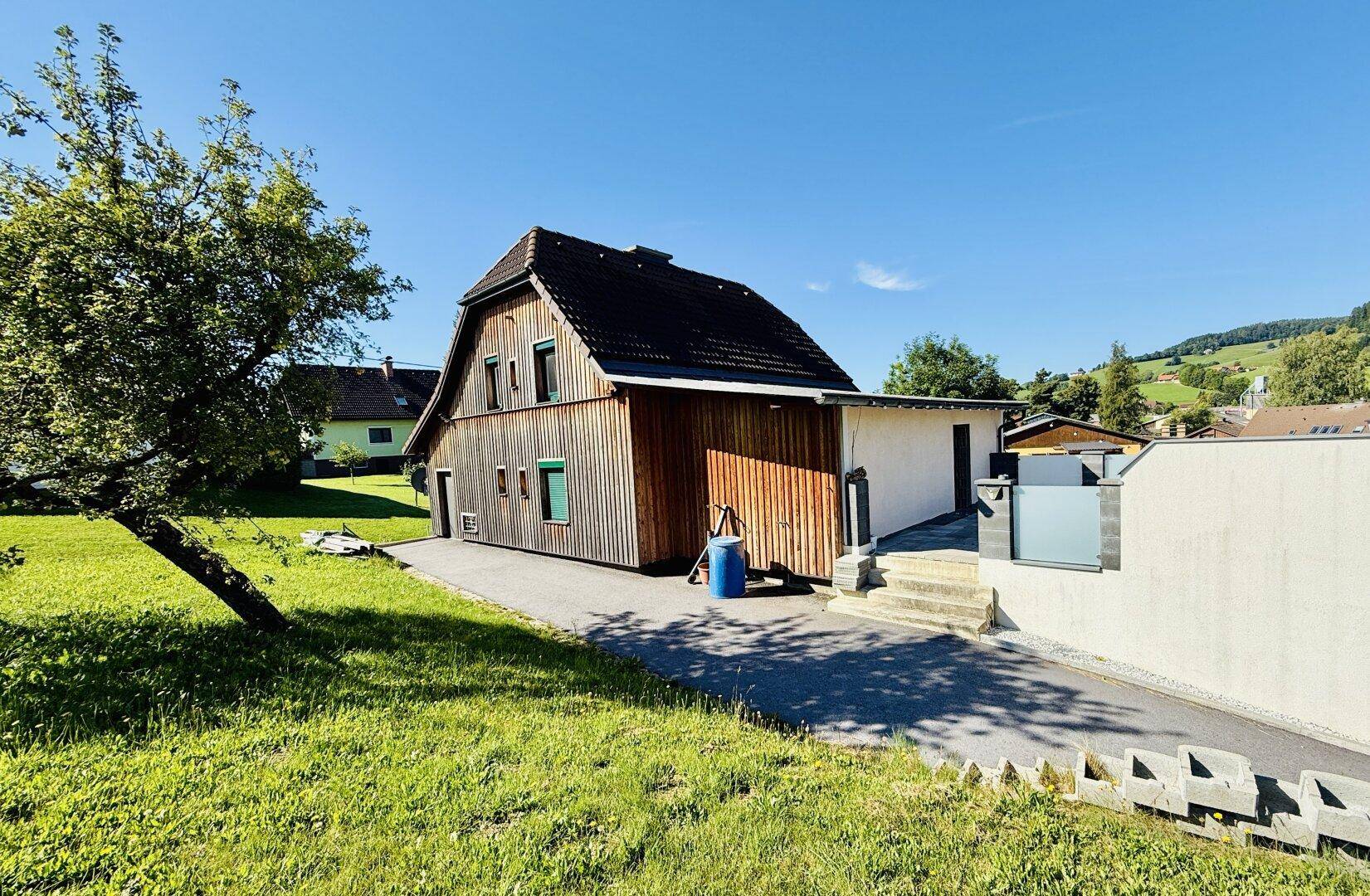 Seitenansicht des Hauses mit Holzverkleidung und großem Gartenbereich unter blauem Himmel.