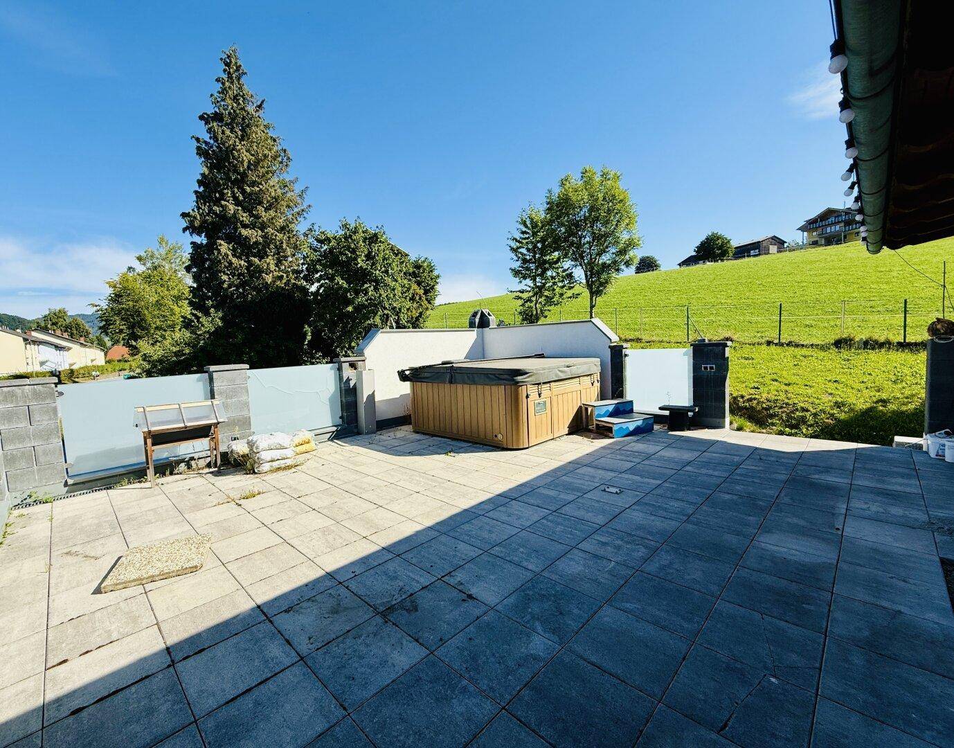 Geräumige Terrasse mit Whirlpool und Blick auf die umliegende grüne Landschaft.