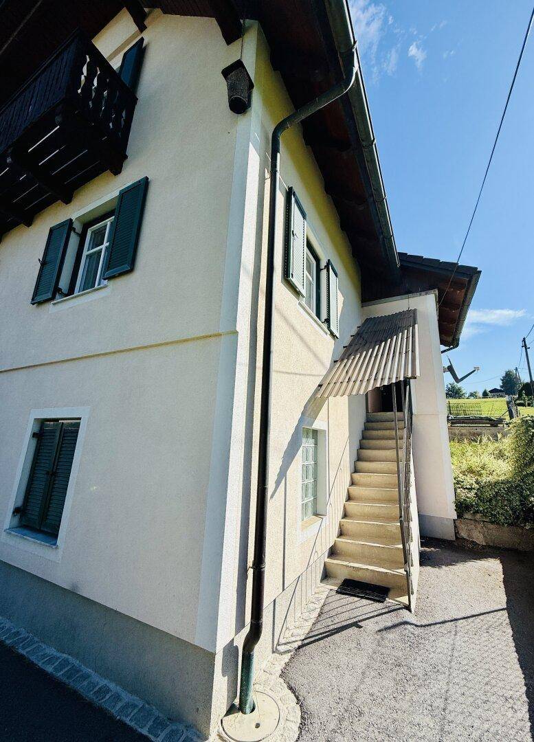 Seitenansicht des Hauses mit Außentreppe und traditionellen grünen Fensterläden.