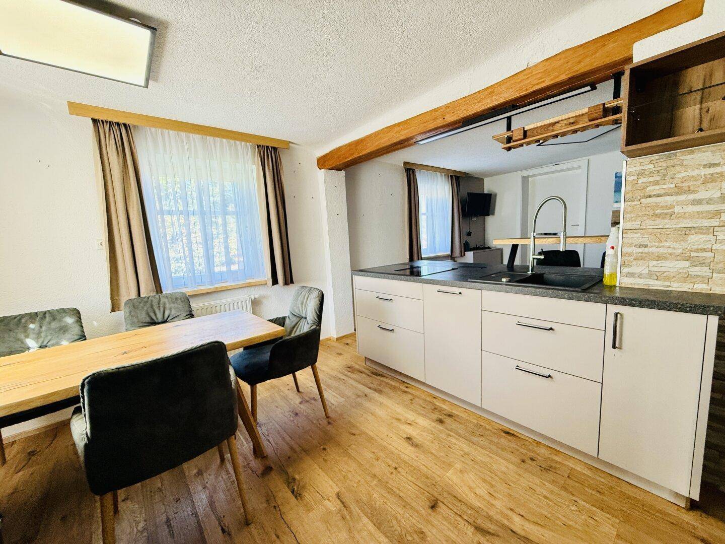 Offene Küche mit Holzbalken, Essbereich und modernen Schränken in hellem Ambiente.