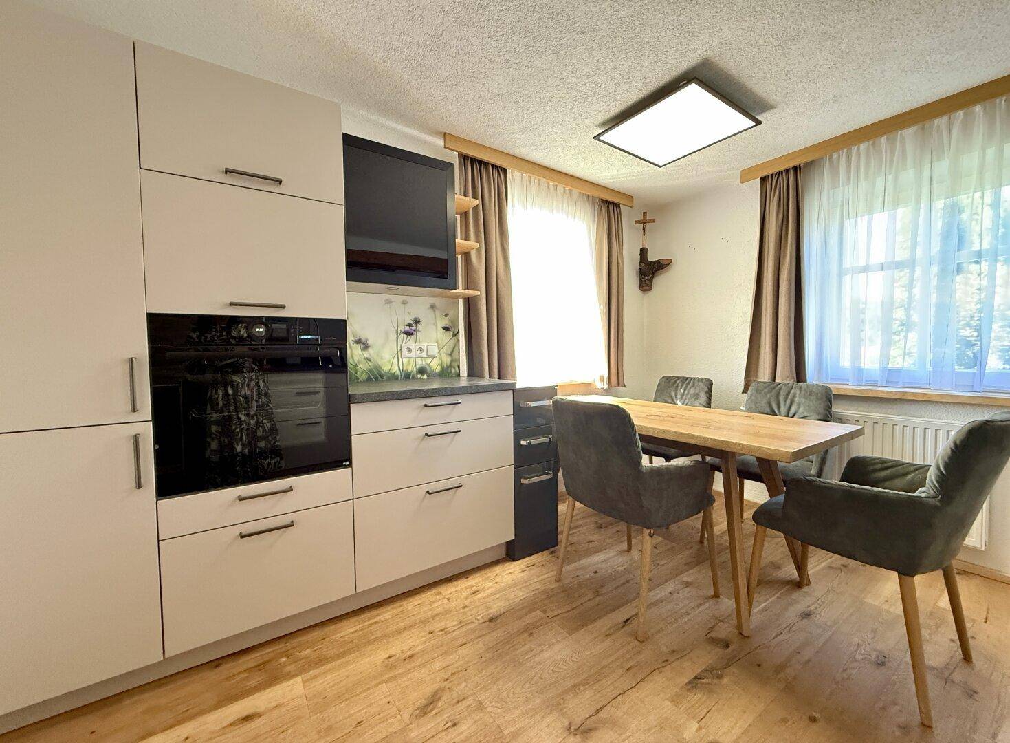 Moderne Küche mit integrierten Geräten, Esstisch und Blick ins Grüne durch das Fenster.