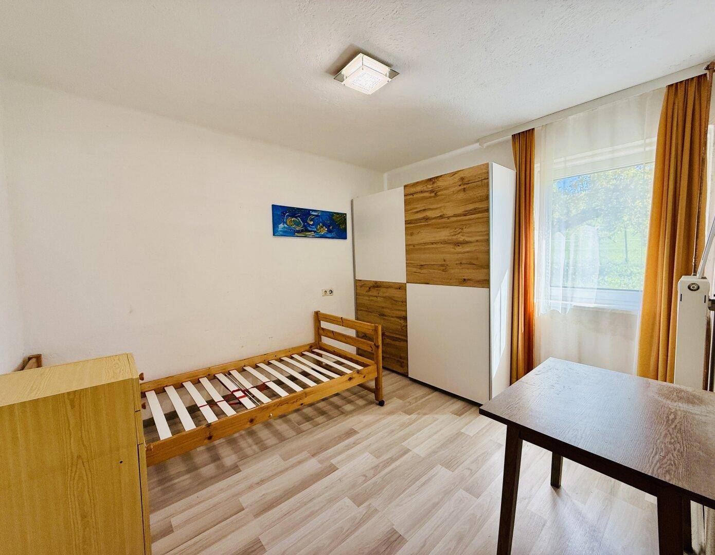Helles Schlafzimmer mit Einzelbett, Kleiderschrank und Laminatboden.