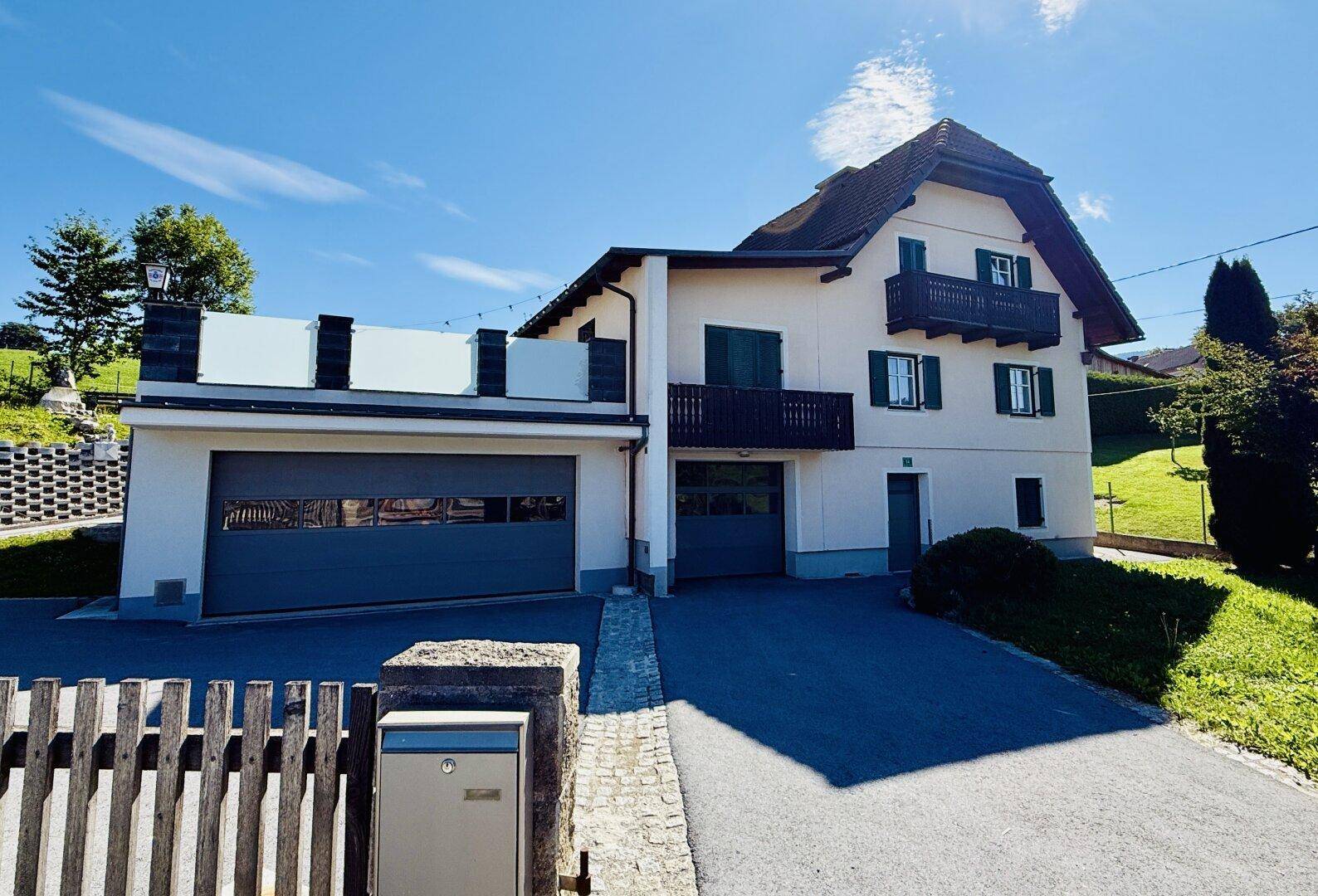 Vorderansicht des Hauses mit zwei Garagen, Balkonen und traditionellen grünen Fensterläden.