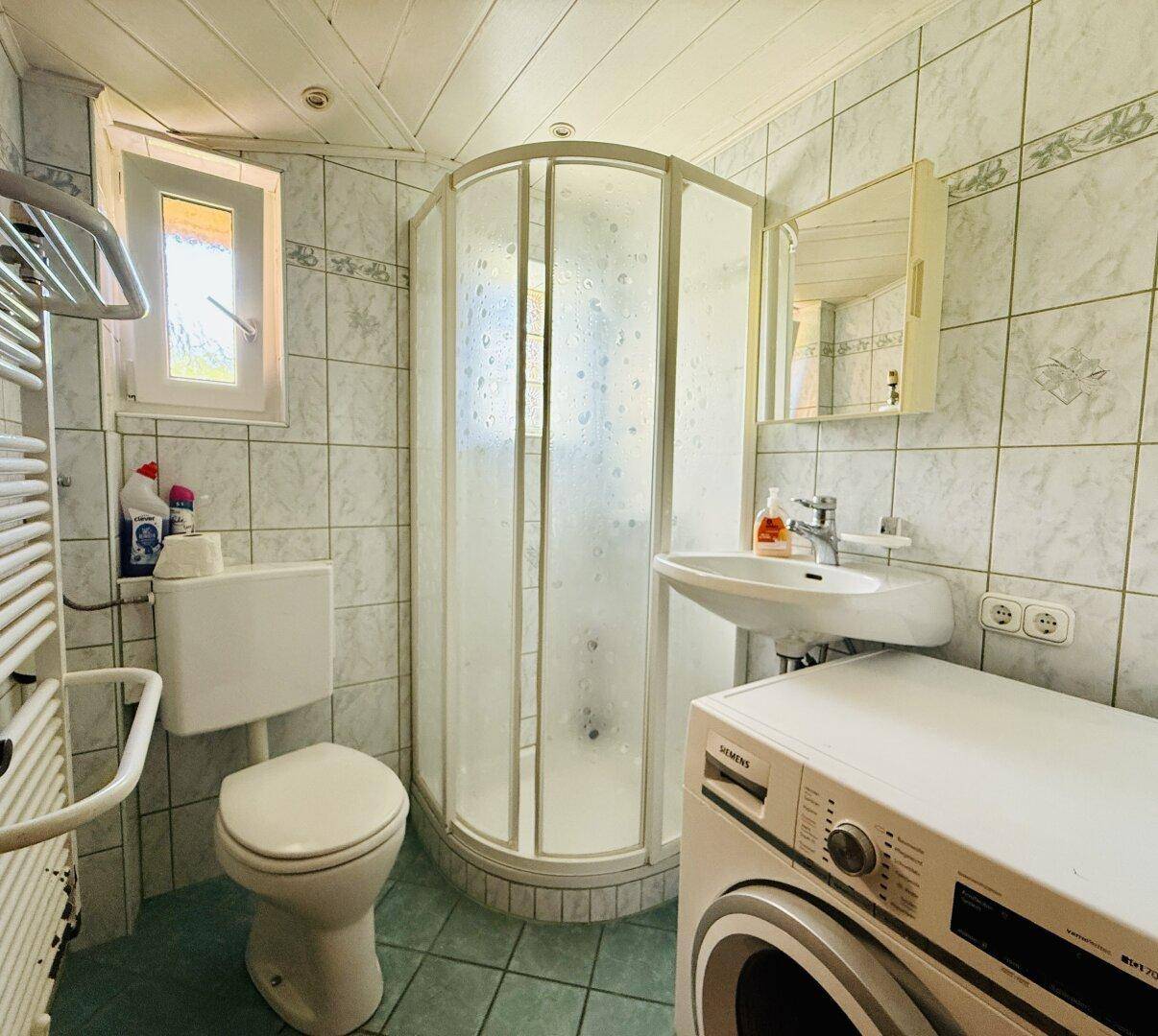 Funktionales Badezimmer mit Duschkabine, WC, Waschbecken und Waschmaschine.