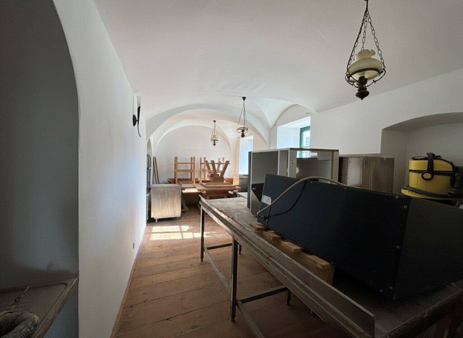Langer Raum mit gewölbten Decken, Holzboden und verschiedenen Gegenständen, möglicherweise ein Lagerbereich, der renoviert werden muss.
