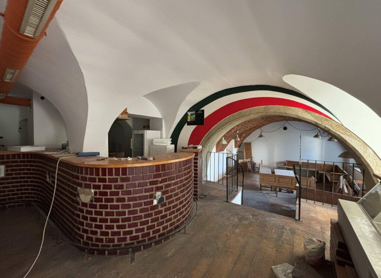 Innenraum eines Restaurants oder einer Bar mit gewölbten Decken, einer Ziegeltheke und sichtbaren Bögen, die renovierungsbedürftig sind.